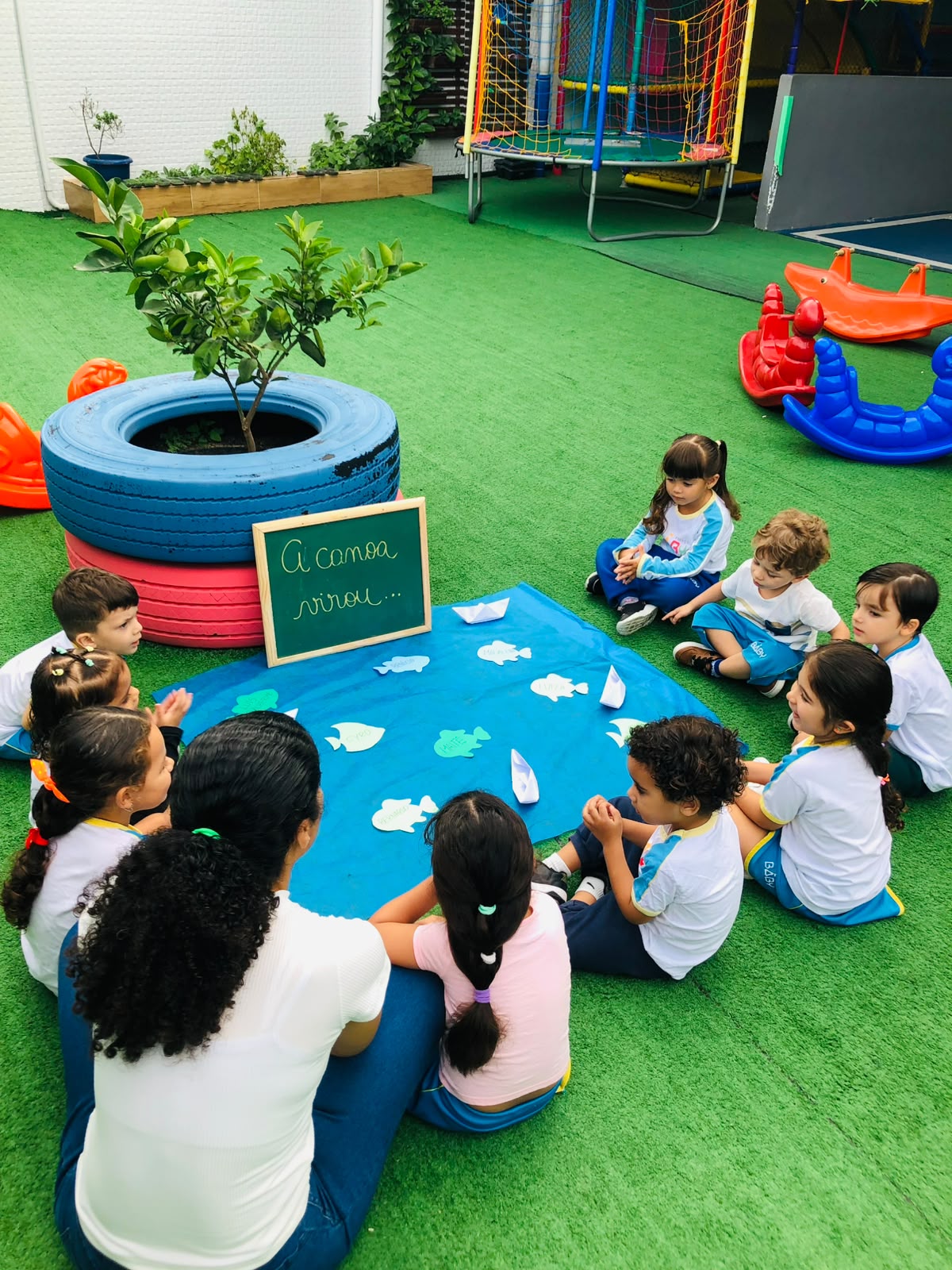 Turma da Espaço Baby em atividade pedagógica ao ar livre, entre plantinhas e brinquedos do pátio